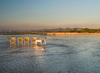 Picturesque dining setup in the shallows of the water with a view of the mountains and blue sky opening up behind in Lusaka, Zambia