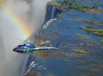 An overhead view of Victoria Falls from the air with a helicopter and a rainbow in the same shot, Zambia