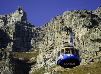 Blue and orange cable car ascends towards the top of Table Mountain with the deep blue sky visible in Cape Town, South Africa