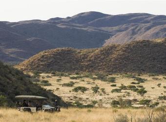 Safari vehicle surrounded by nothing but African wilderness in the form of plains, grasslands, and mountains in southern Kalahari, South Africa