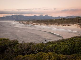 The coast stretches out as far as the eye can see next to the looming mountains in the far distance scraping the heavens in Cape Cost, South Africa